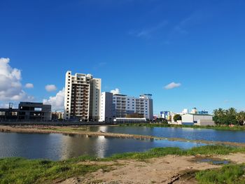 Buildings by river against blue sky