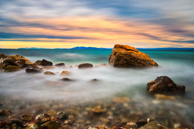 Rocks on beach against sky during sunset