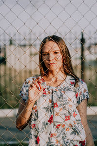 Portrait of woman standing by chainlink fence