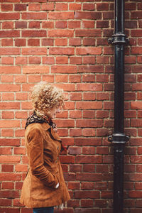 Side view of woman with hand in pocket standing by brick wall