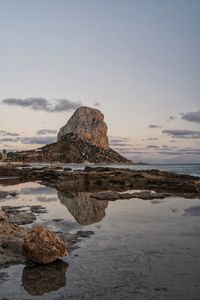 Rock formation on beach against sky during sunset