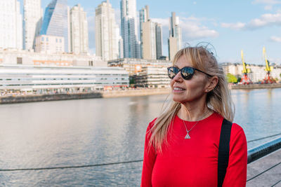 Mature woman with sunglasses looking the horizon. in the background office building. selective focus