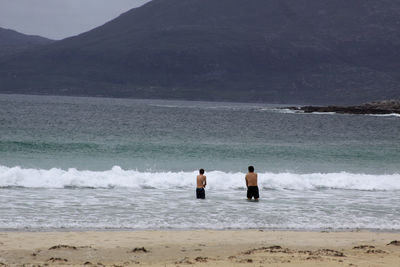 Men standing in sea against mountain