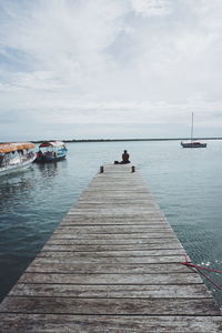 Person sitting on pier over sea against sky