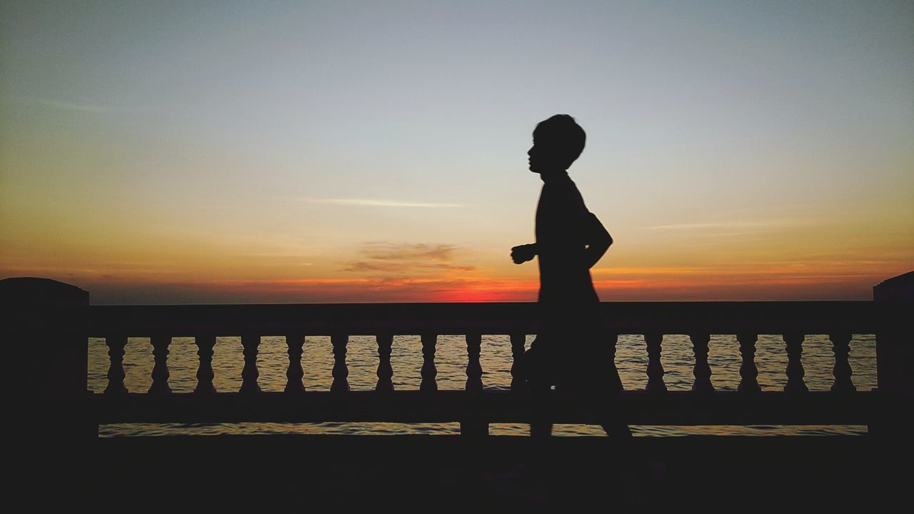 sunset, silhouette, railing, sky, water, orange color, standing, sea, lifestyles, full length, men, leisure activity, bridge - man made structure, nature, tranquility, scenics, beauty in nature, rear view