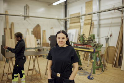 Portrait of female carpenter standing with hands in pockets at workshop