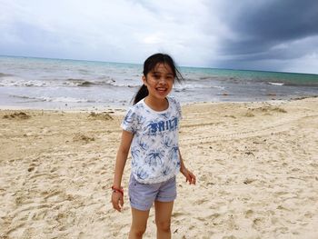 Portrait of happy girl standing on beach against sky