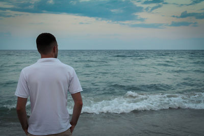 Rear view of man standing at beach against sky