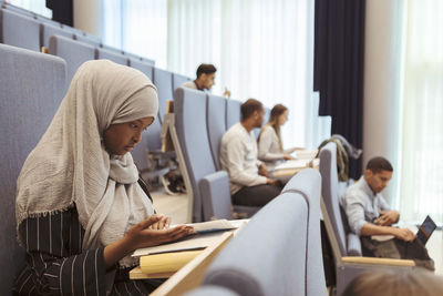 Serious woman in hijab reading book by students at university lecture hall