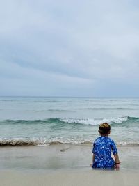 Rear view of woman standing at beach against sky