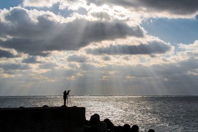 Silhouette people standing on beach against sky during sunset