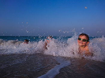 Boys swimming in sea against clear sky during sunset