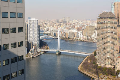 Aerial view of suspension bridge across sunny sumida river ans skyscrapers in spring tokyo