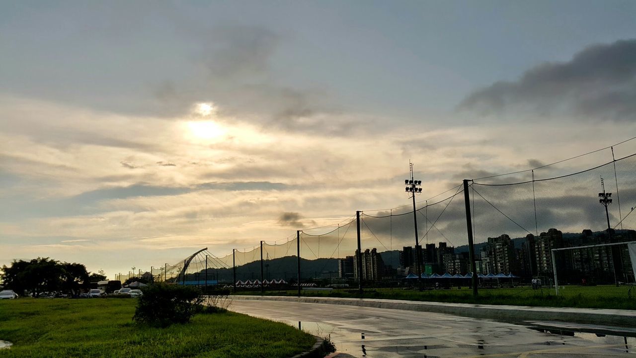 sky, cloud - sky, street light, built structure, tree, architecture, building exterior, road, transportation, cloud, the way forward, grass, cloudy, sunlight, street, outdoors, footpath, connection, nature, electricity pylon