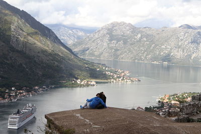 Rear view of man sitting by lake against mountains