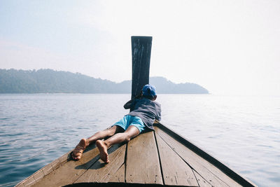 Man sitting on wood against sea against sky