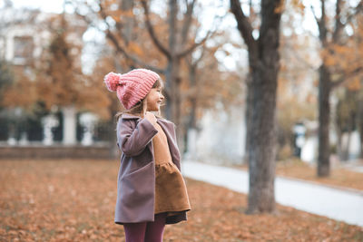 Happy smiling child 4-5 year old wear jacket and hat in park with fall leaves over nature background