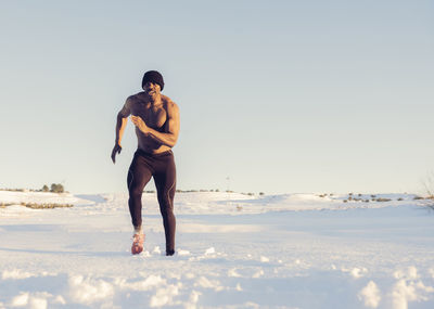 Shirtless athlete exercising while running in snow during sunset