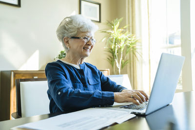 Senior woman smiling while using laptop computer at home