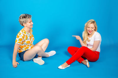 Full length of a smiling boy sitting against blue wall