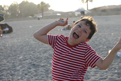 Boy laughing while standing on sand at beach during sunset