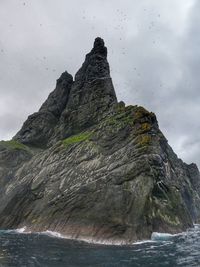 Rock formation by sea against cloudy sky