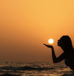 Optical illusion of silhouette woman holding sun against sea during sunset