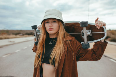 Portrait of beautiful young woman standing by car against sky