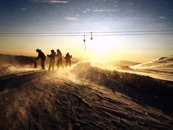 People skiing on mountain against sky during sunset