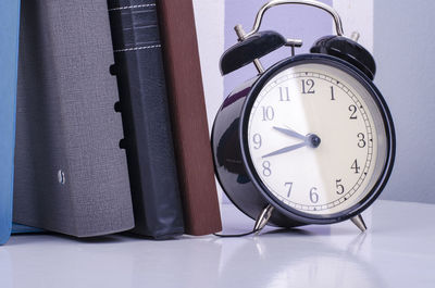 Close-up of alarm clock by diaries on table against wall