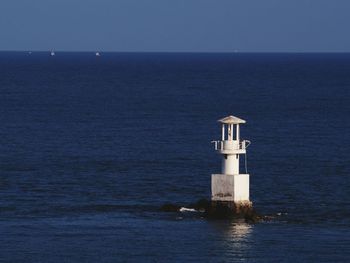 Lighthouse by sea against clear sky