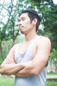 Young man with arms crossed listening music while standing on field