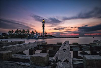 Wooden pier over sea against lighthouse during sunset