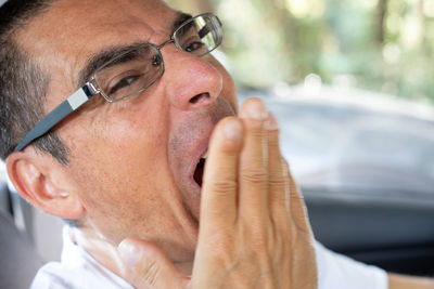 Close-up portrait of man yawning in car