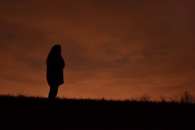 Silhouette of woman standing on field at sunset