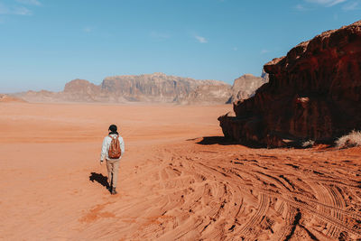 Rear view of man on rock in desert against sky