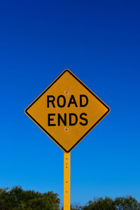 Low angle view of road sign against clear blue sky