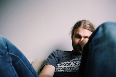 Tired man sitting on sofa by white wall at home