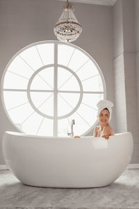 Smiling woman sitting in bathtub by window