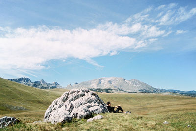 Side view of man sitting by rock against sky