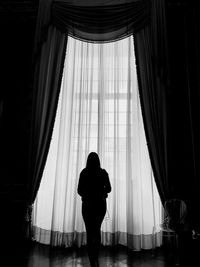 Rear view of silhouette woman standing by window in darkroom