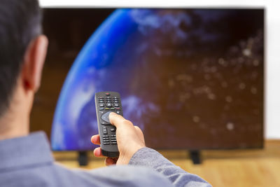 Rear view of man holding remote control while watching television