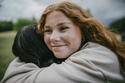 Smiling teenage girl embracing female friend at park