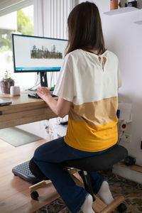 Rear view of woman using mobile phone at home