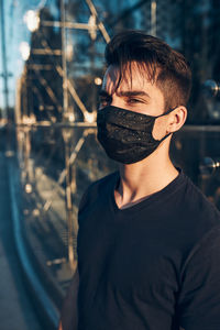 Young man standing in the city center at glass store front in the evening looking away