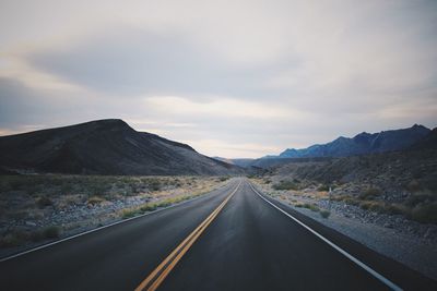 Road leading towards mountains against cloudy sky