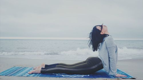 Side view of woman practicing upward facing dog position while exercising on shore at beach