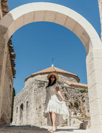 Low angle full length image of young woman wearing white dress standing in stone street in old town.