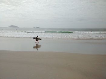 Surfer walking at beach against sky