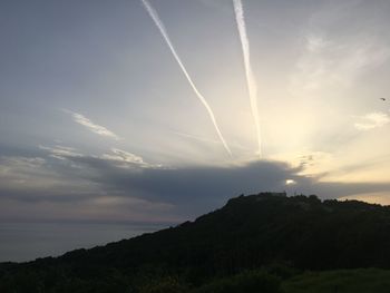 Low angle view of vapor trails in sky at sunset